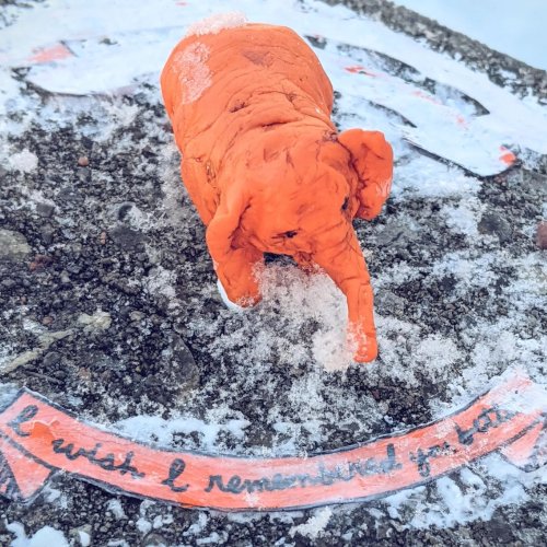 Photograph of a bright orange sculpture of an elephant. There is a bit of painted paper beneath, in the same orange, which says, 'I wish I remembered you...' and then is obscured by snow.